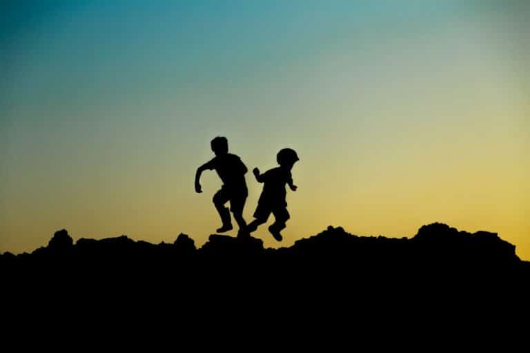 צלליות של שני ילדים משחקים על גבי הר