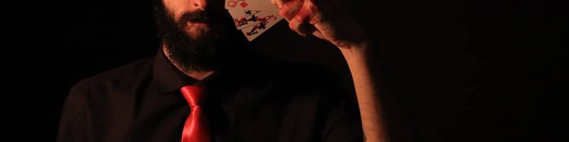 איש עם זקן שחור ועניבה אדומה מחזיק עשרה קלפים